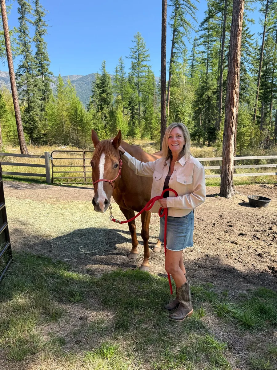 Amy Stevens smiling beside a chestnut horse at a Montana horse property